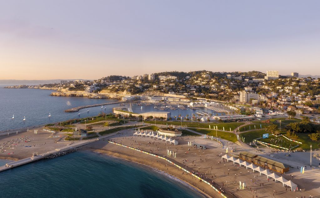 Vue aérienne du Stade Nautique du Roucas Blanc à Marseille, projet proposé par Chabanne Archi Ingé dans le cadre du concours pour la transformation du site des épreuves de voile des JO 2024 de Paris, illustrant les différents bâtiments de la marina aux volumes bas et horizontaux, aux toitures végétalisées, répartis autour des espaces nautiques et reliés par une trame de cheminements paysagers ouverts sur le parc, la plage et la mer.