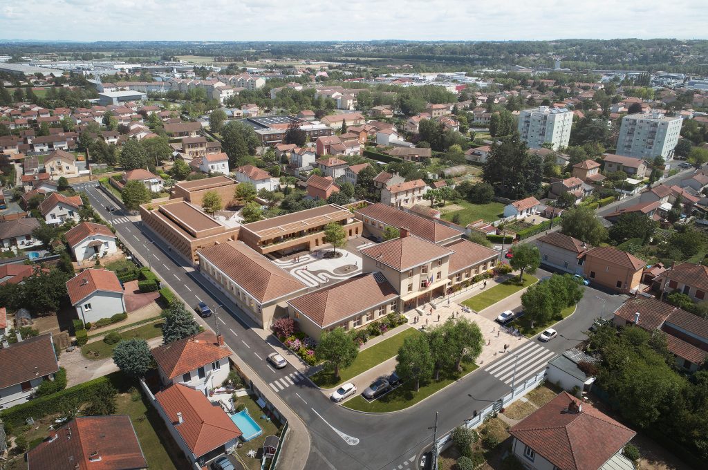 Vue aérienne du concours pour le futur groupe scolaire Jean Macé à Villefranche-sur-Saône, projet lauréat conçu par NTSA, montrant l'insertion des bâtiments neufs en pisé de terre crue locale et réhabilités, reliés par des motifs primitifs au sol jusqu'au parvis.
