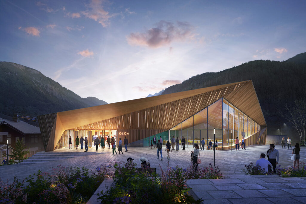 Vue de nuit de l'Espace OLCA aux Houches, projet lauréat conçu par MILK Architectes, montrant le nouveau volume rétroéclairé à l'architecture signal formant un monolithe émergeant du paysage alpin pour unifier le bâtiment existant et son extension par le prolongement des toitures en bois.